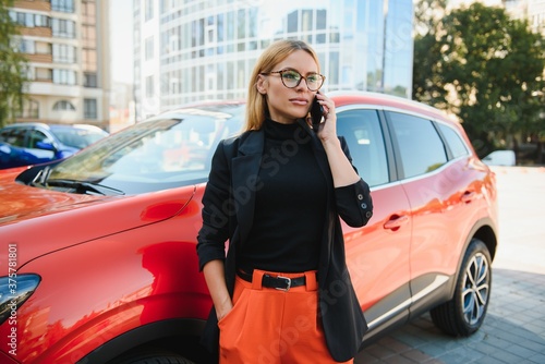 Woman using mobile phone, communication or online application, standing near car on city street or parking, outdoors. Car sharing, rental service or taxi app. © Serhii