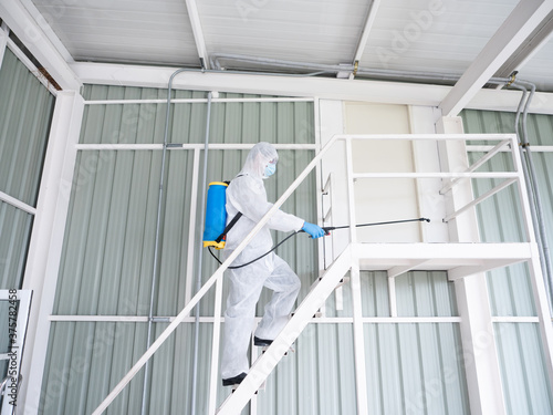 Cleaner man going to upstairs and using sanitizer spray with chemical sterilize in backpack for Covid-19 disease and vius prevention in warehouse industry while wearing face mask and hygiene uniform photo