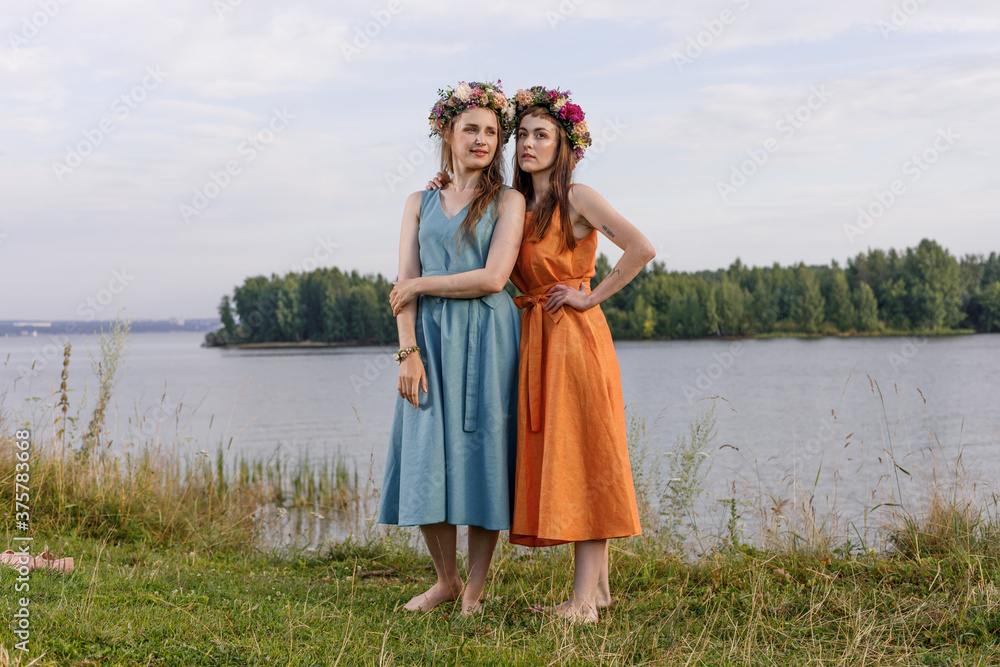 Two young and lovely girls in flower wreaths in nature. Ancient pagan origin celebration concept. Summer solstice day. Mid summer. Ancient rituals. Two young and lovely girls in flower wreaths in nature. Ancient pagan origin celebration concept. Summer solstice day. Mid summer. Ancient rituals.