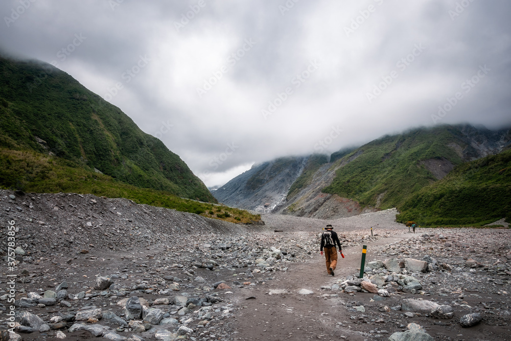 Active middle-aged man hiking through rugged terrain on the trail to the Franz Josef Glacier in the Southern Alps of New Zealand, one of the iconic destinations in the Southern Island.