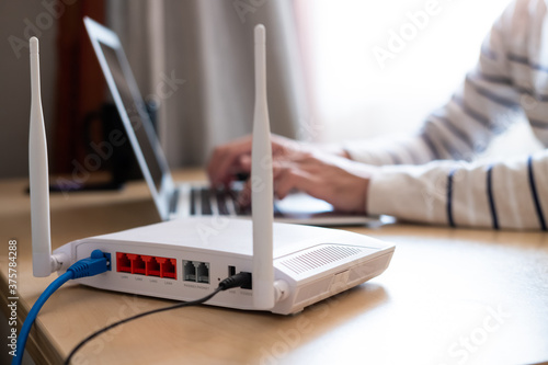 Selective focus at router. Internet router on working table with blurred man connect the cable at the background. Fast and high speed internet connection from fiber line with LAN cable connection. photo