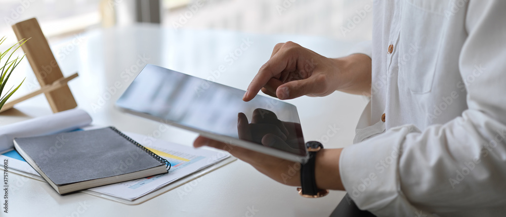 Close-up view of young businessman working on his company plan while using tablet in office