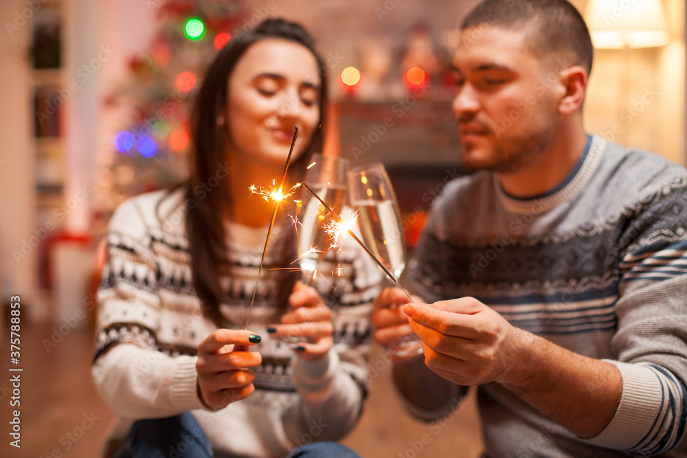 Happy couple clinking glasses of champagne and holding hand fireworks on christmas.