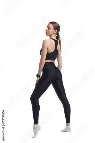 Slender athletic girl gymnast in black sportswear stands in full growth isolated on a white background view from the back.