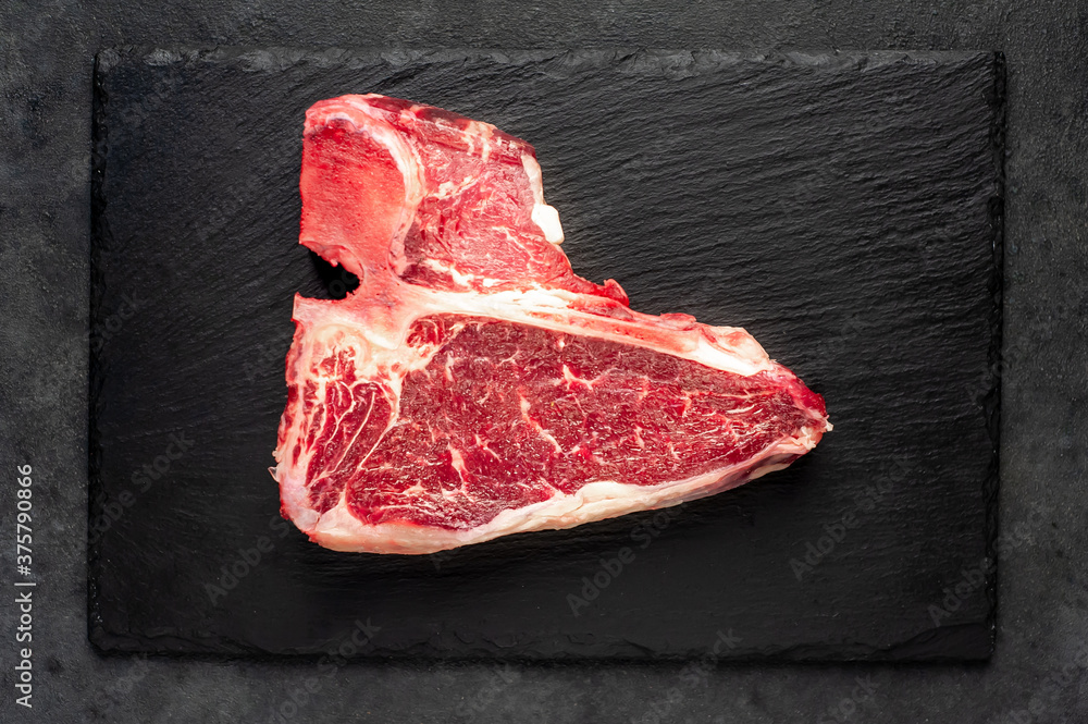 raw t-bone steak with  on stone background