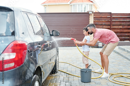 Young adult father and his little son washing car, horizontal side view shot, copy space photo