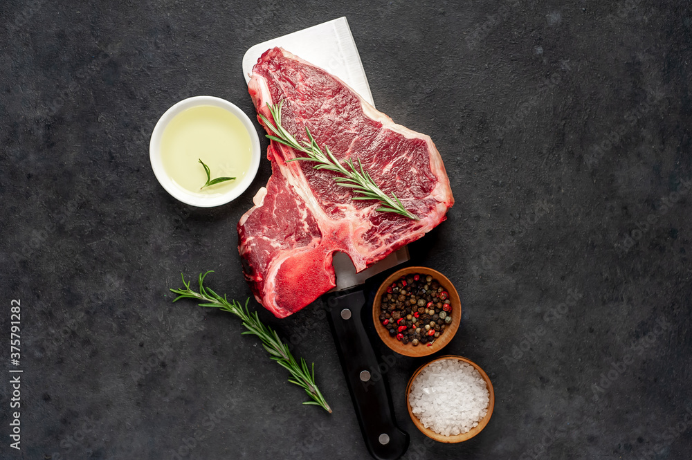 raw t-bone steak with ingredients on a meat knife on stone  background