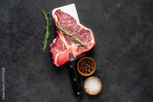 raw t-bone steak with ingredients on a meat knife on stone  background