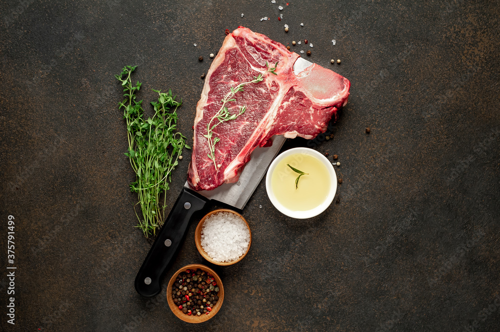 raw t-bone steak with ingredients on a meat knife on stone  background