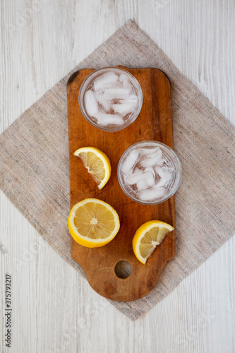 Fresh Lemon Sparkling Water with Ice on a rustic wooden board on a white wooden background, overhead view. Top view, from above, flat lay.