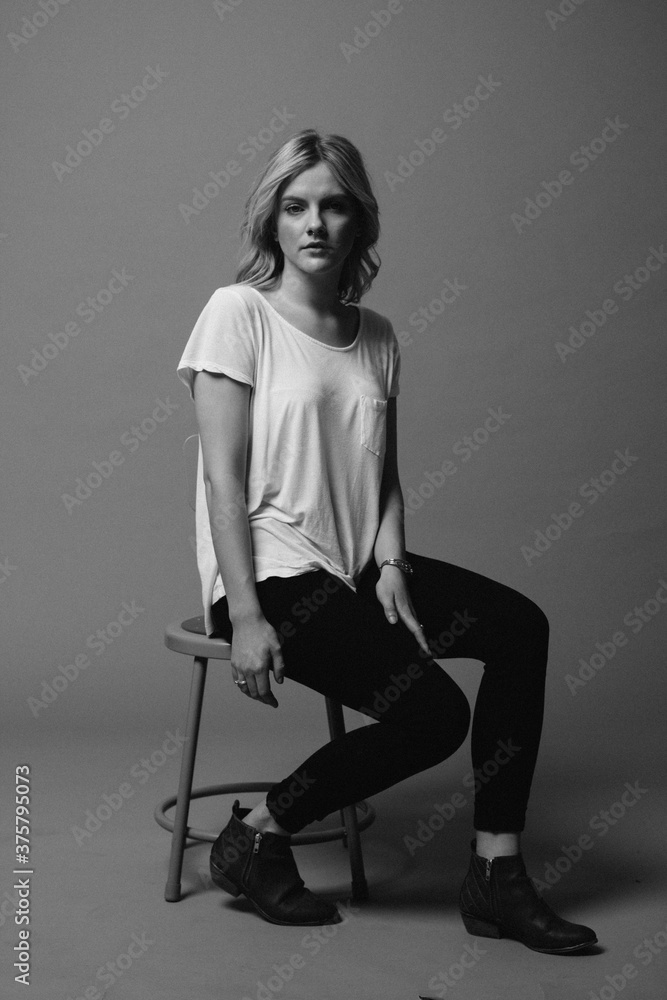 black and white moody portrait of female in studio on stool black and white moody portrait of female in studio on stool