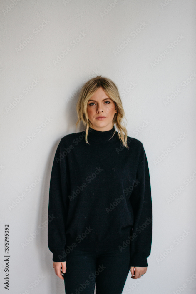 Young blonde female wearing dark sweater in front of white wall Young blonde female wearing dark sweater in front of white wall