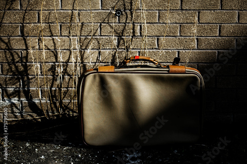 Old abandoned suitcase creeping out of the shadows against a brick wall. photo