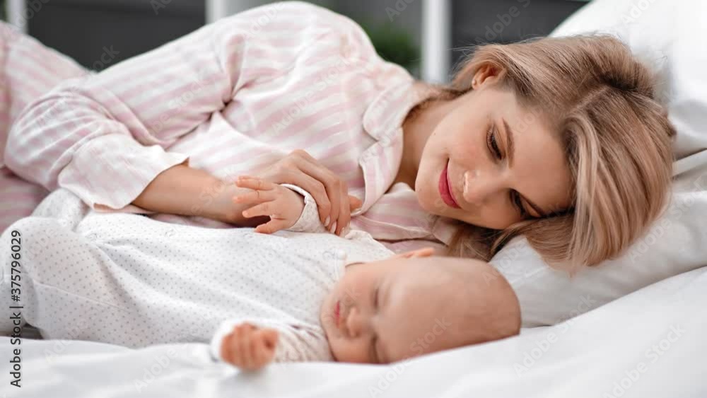 Happy mother admiring cute sleeping baby lying on bed together. Shot on RED Raven 4k Cinema Camera Happy mother admiring cute sleeping baby lying on bed together. Shot on RED Raven 4k Cinema Camera