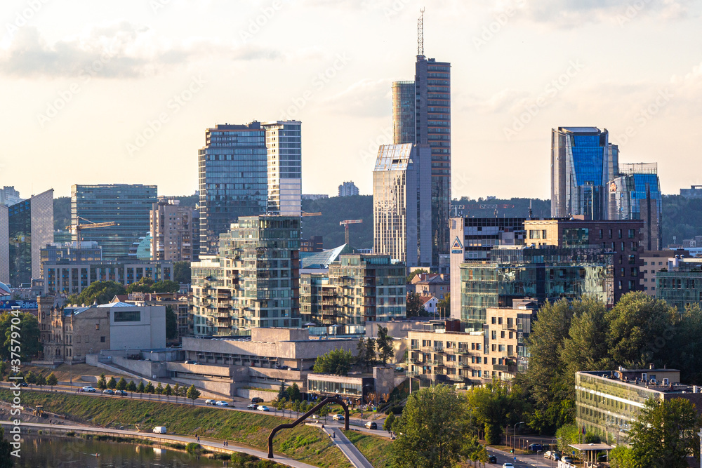 Naklejka premium anorama of Vilnius at sunset in August 2020. City buildings. Skyscrapers on the horizon. Blue sky over the city. Clouds and sun at sunset. Summer evening. A quiet day at the weekend