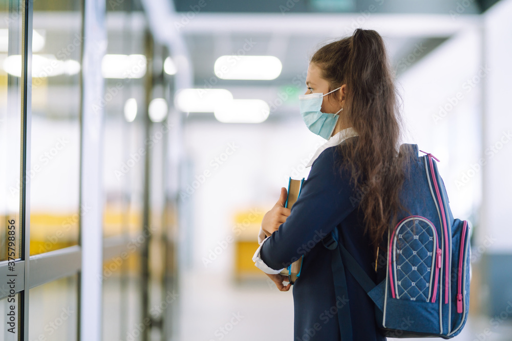 Schoolgirl in a protective mask with a backpack and a textbook in her hands. Security concept, virus protection. Covid-2019.