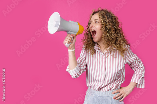 Young woman shouts into a megaphone. Isolated pink background.