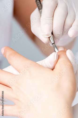 Hands of manicurist pushing cuticles on female s nails with manicure tool. Woman receiving manicure and nail care procedure