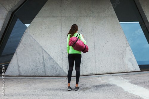 Back view of a young woman holding a sportbag outside in the city. photo