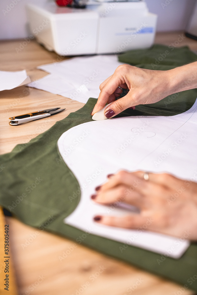 Selective focus of seamstress marking cloth near layout in workshop 