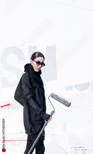 Beautiful female artist in neo outfit with paint roller in front of white abstract wall. photo