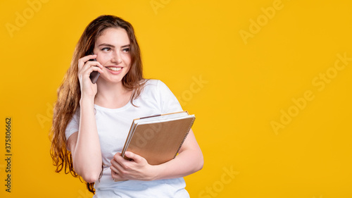 Business call. Advertising background. Portrait of cheerful happy woman in white with notebooks talking on phone smiling isolated on orange copy space. Project management. Professional course.