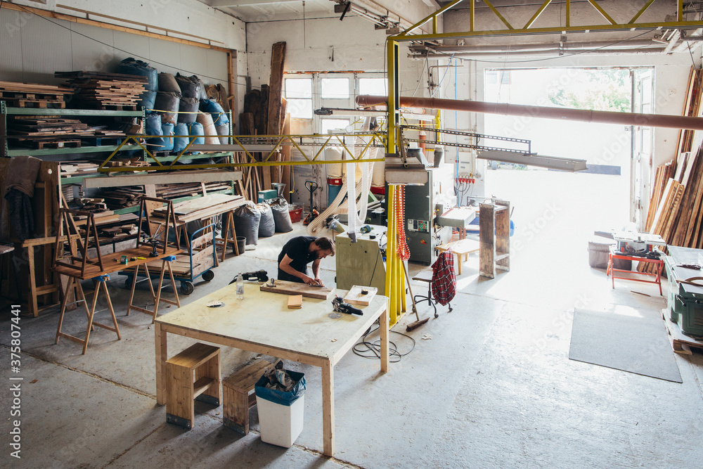 Carpentry - Young Man Doing Woodwork in Large Bright Industrial Workshop Carpentry - Young Man Doing Woodwork in Large Bright Industrial Workshop