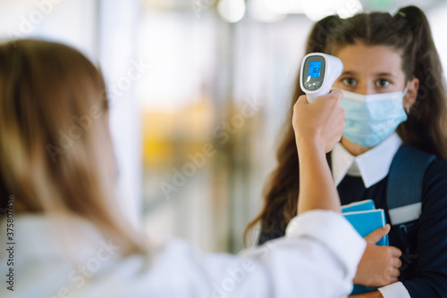 Nurse or doctor checks Schoolgir body temperature using infrared forehead thermometer (gun) for virus symptom - epidemic outbreak concept. Back to school in quarantine. Covid-19.