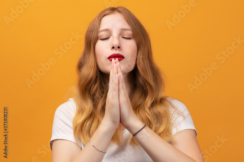 Pretty girl with wavy redhead, holding palms together, praying for peace and love, having peaceful facial expression