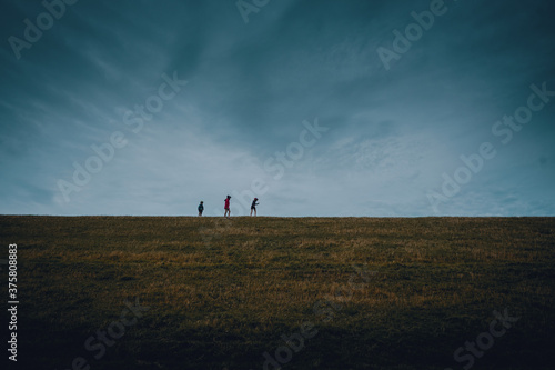 Drei Kinder laufen hintereinander auf dem Grad eines Deichs in Ostfriesland
