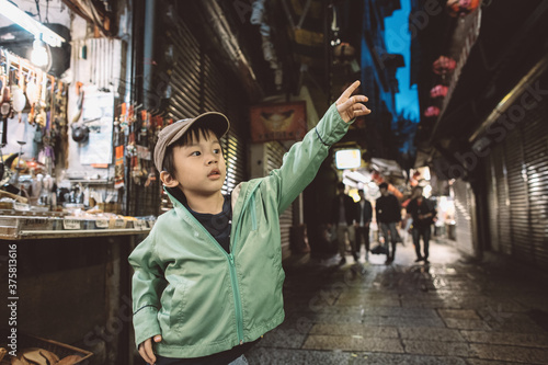 Little kid wearing cap and jacket pointing upwards while standing along a market street photo