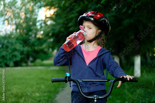 Little girl drinking water by the bike. Child in helmet riding a bicycling.