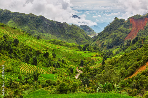Wide view of a valley with rice paddies in the morning with a cloudy sky.