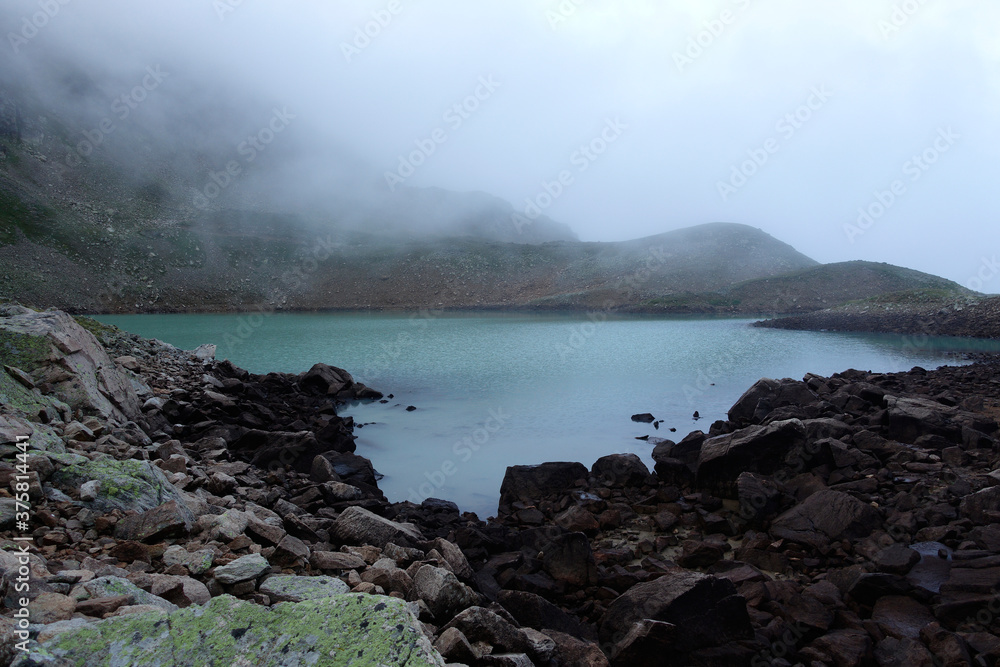 Alpine lake in the clouds. Alpine lake with rocky shores and emerald water in the clouds. Alpine lake Giybashkel (3240 meters above sea level), Caucasus. 