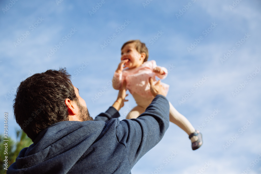 Young man father playing with his baby girl daughter throwing her in the air with blue sky background Young man father playing with his baby girl daughter throwing her in the air with blue sky background