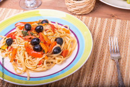 Vegetarian pasta with vegetables, linguine with bell pepper, tomatoes and olives on a plate standing on a napkin on the table - a close-up