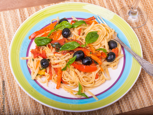 Vegetarian pasta with vegetables, linguine with bell pepper, tomatoes and olives on a plate standing on a napkin on the table - a close-up