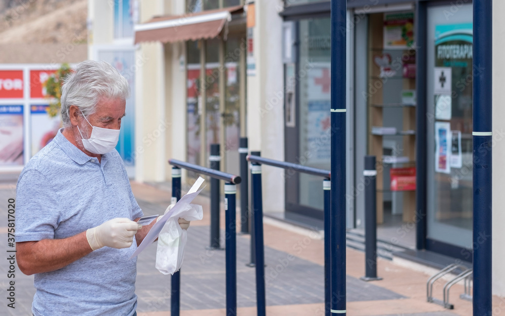 Senior man white haired wearing medical mask and protective gloves to prevent coronavirus infection goes to pharmacy - new normal concept