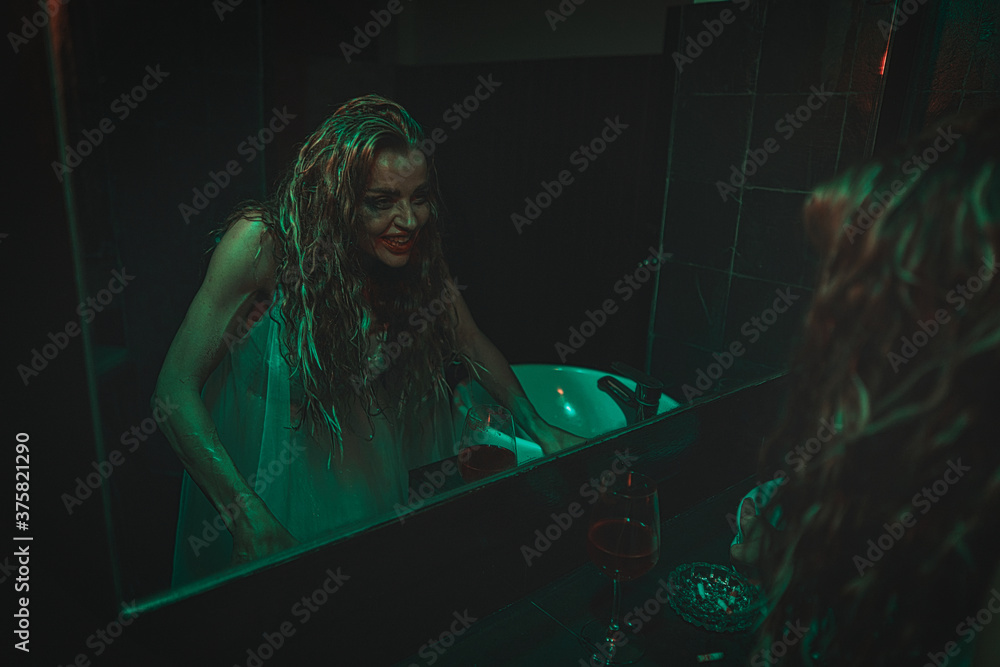 mysterious woman wearing wedding dress looking at her scary reflection in a mirror.