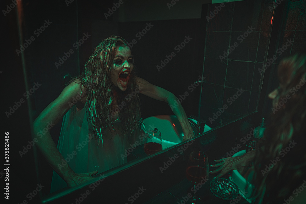 mysterious woman wearing wedding dress looking at her scary reflection in a mirror.
