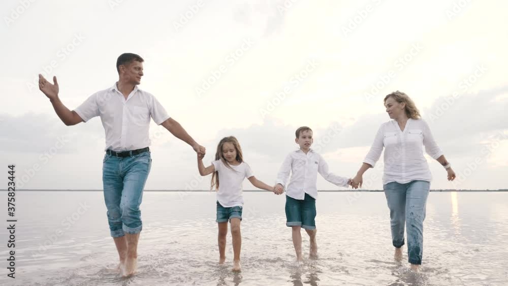 Excited smiling caucasian family walks on lake water discussing vacation together holding hands. Funny journey, summer relax, leisure happiness of loving talking couple with carefree children outdoors Excited smiling caucasian family walks on lake water discussing vacation together holding hands. Funny journey, summer relax, leisure happiness of loving talking couple with carefree children outdoors
