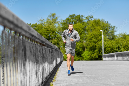 fitness  sport and healthy lifestyle concept - happy young man running across city bridge