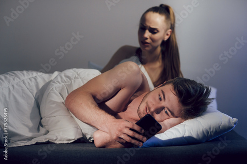 The concept of relationships and betrayal in the family. The man, lying in bed, corresponded on mobile phone with his mistress. The wife woke up and watching her husband
