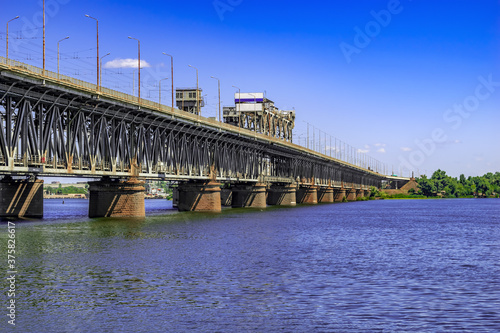 Side view of Amurskyi Bridge over the Dnieper river in Dnipro (Ukraine) on a sunny summer day. Landscape with an old metal bridge and powerful stone pillars. Architectural background with copy space