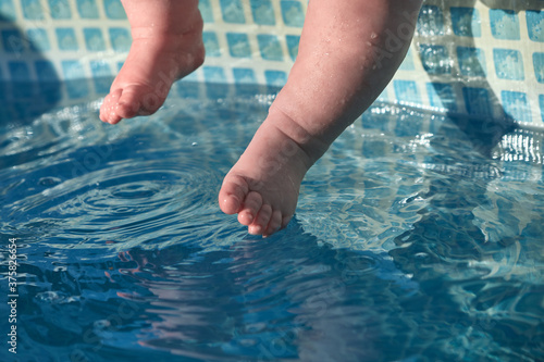 Baby's feet touch the blue water in the pool. Concept of newborn swimming training.