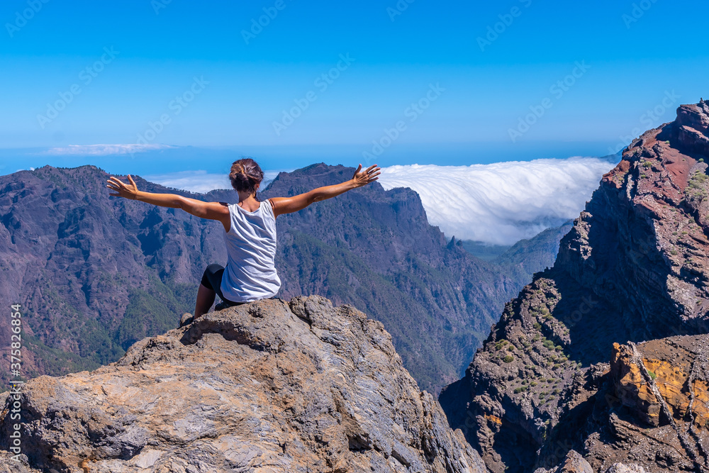 A young woman sits resting and looking at the views of the Roque de los Muchachos national park on top of the Caldera de Taburiente, La Palma, Canary Islands. Spain