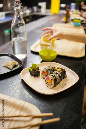 Photography Vertical shot of a korean food restaurant plated kimbap with mandu, water bottle and bokeh elements like chopstics, out of focus hand and beer