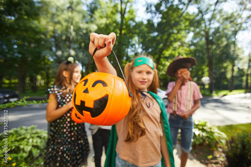 Portrait of girl holding bag in the form of pumpkin with sweets while standing outdoors with her friends