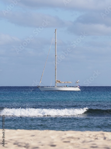 Yacht and white wave of Atlantic Ocean landscapes at african Sal island in Cape Verde, horizon line and clear blue sky in 2019 warm sunny summer day on March - vertical.