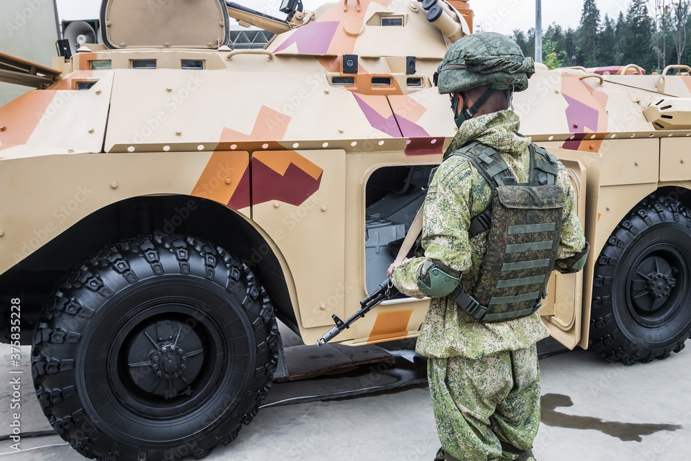 soldier in full armor stands next to military equipment. Modern weapons and military equipment